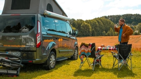 A camper set up at an RV park with chairs and a picnic table in an open field, showing a relaxed outdoor scene perfect for road trips.