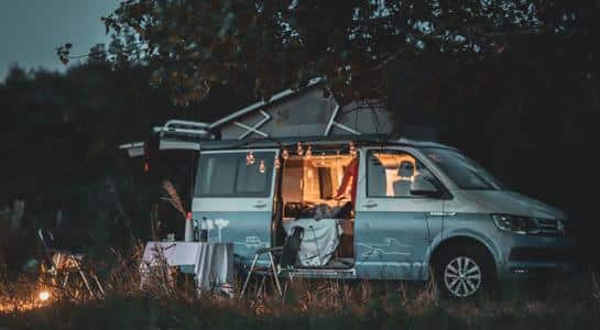 A cozy nighttime RV park setup with a camper lit from inside and string lights creating a warm, inviting atmosphere.