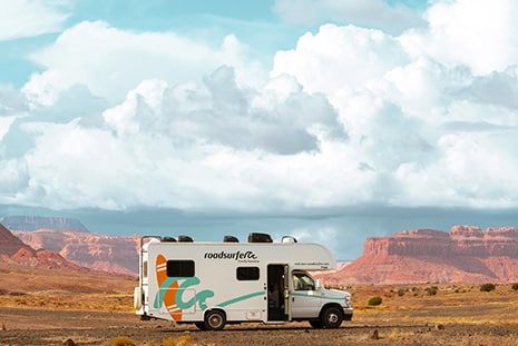 motorhome parked in a vast desert landscape with red rock formations and a sky filled with fluffy clouds