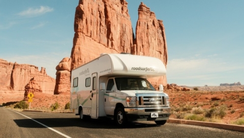 Class C RV driving along a desert highway with towering red rock formations, illustrating RV rentals near me for scenic adventures