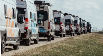 Row of camper vans parked in a line along a rural road under a blue sky, representing RV rentals near me