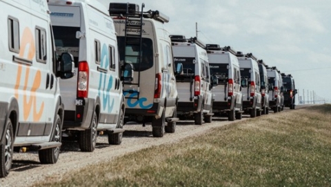 Row of camper vans parked in a line along a rural road under a blue sky, representing RV rentals near me