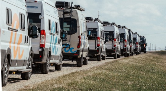 Row of camper vans parked in a line along a rural road under a blue sky, representing RV rentals near me