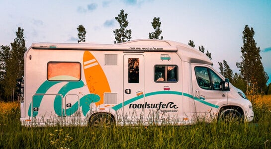 Motorhome with roadsurfer wrapping standing on a field at sunset