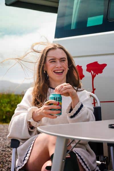 A woman enjoying a drink outside her RV at an RV park during a road trip, showing the relaxed atmosphere common at many rv parks.