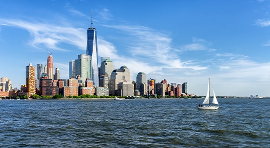 Tiny sailboat on sailing towards the skyline of New York City.