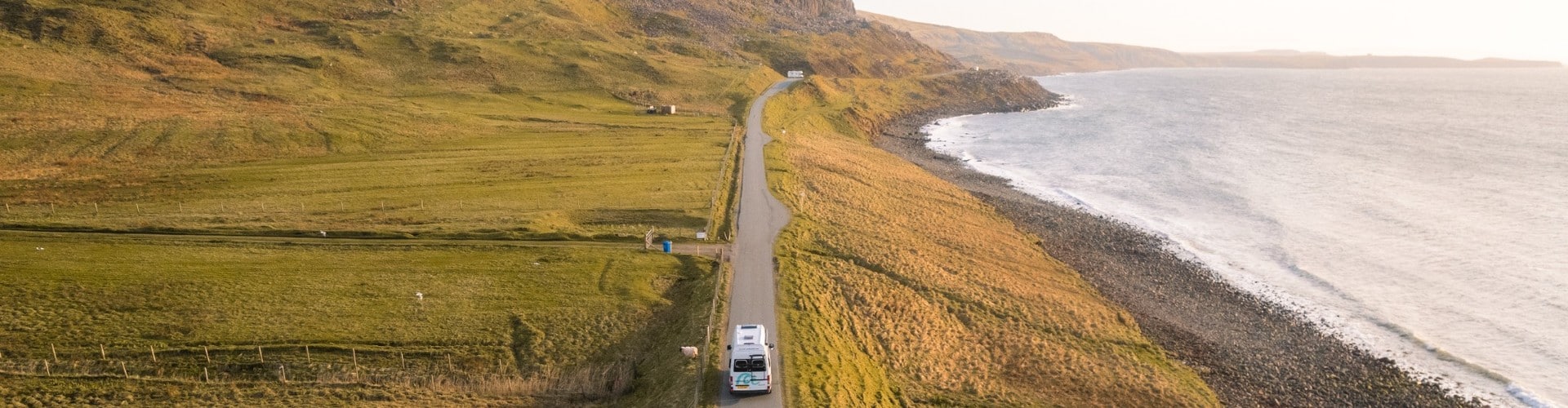 RV driving along a scenic coastal road at golden hour during a Scotland Highland road trip, with dramatic cliffs and the sea in view.