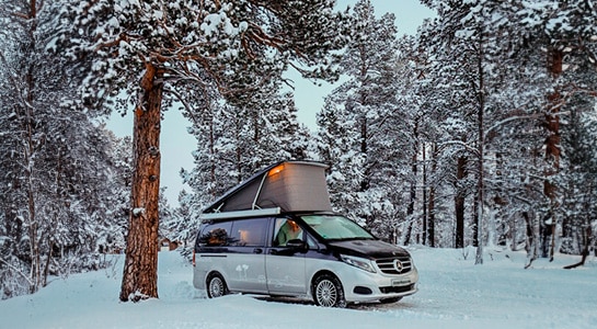 silver camper van with pop up roof in a cozy winter landscape