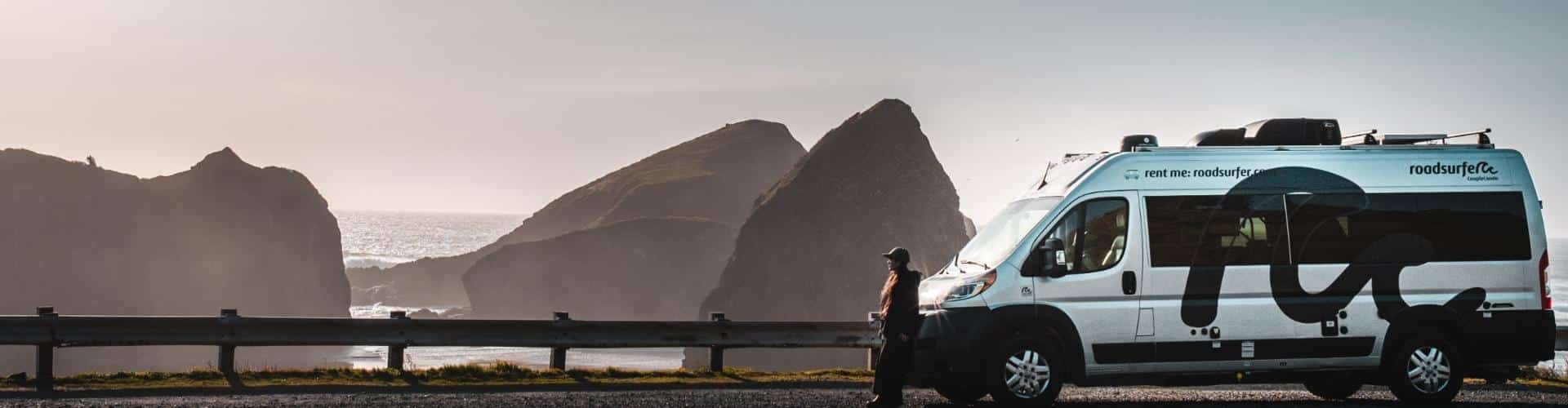 A small RV rental parked along a scenic coastal viewpoint with rocky formations in the background.