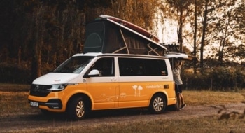 Small RV rental camper van parked at sunset with the pop-top open and a traveler loading gear