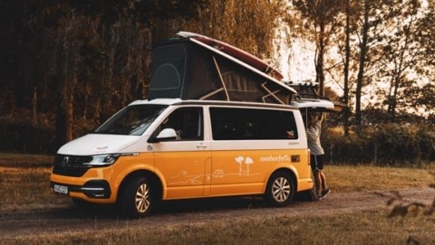Small RV rental camper van parked at sunset with the pop-top open and a traveler loading gear
