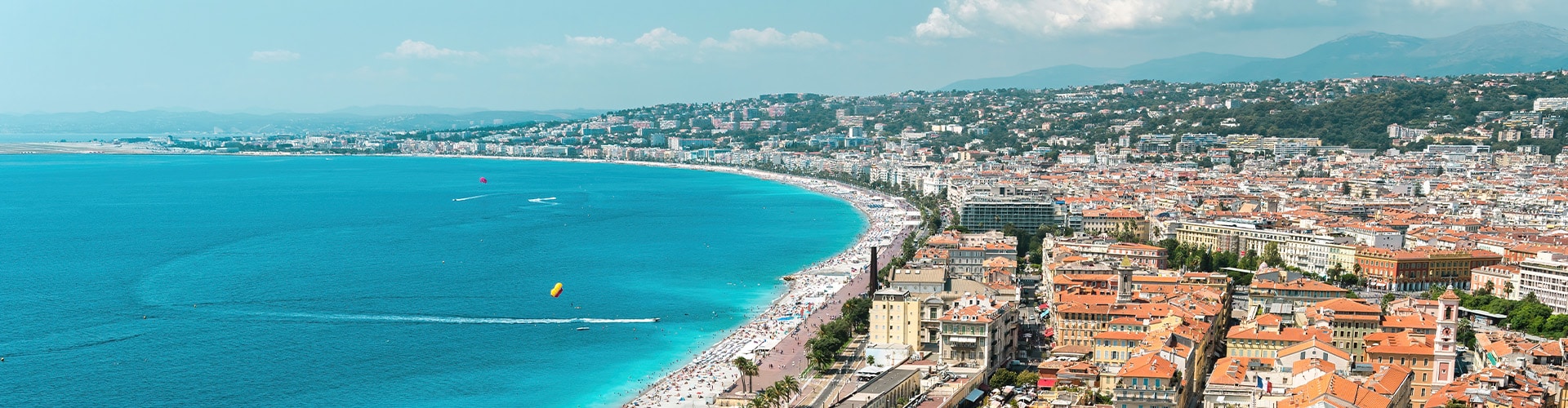 Coastal View over a city in South of France showing the sea to the left, the beach in the middle and the city to the right. In the back one can see mountains.