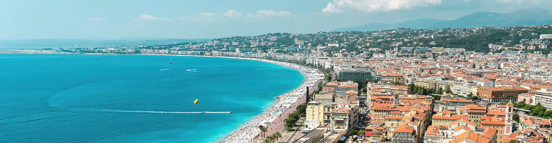 Coastal View over a city in South of France showing the sea to the left, the beach in the middle and the city to the right. In the back one can see mountains.