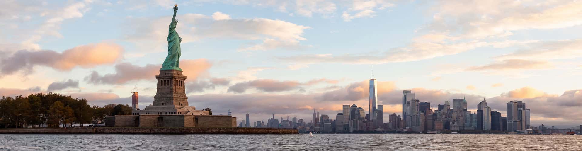 Statue of Liberty in New York seen from the water with the skyline of New York City in the background.