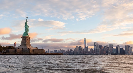 Statue of Liberty in New York seen from the water with the skyline of New York City in the background.