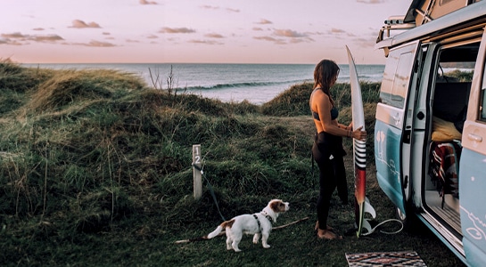 surfer girl with her dog and camper near the sea