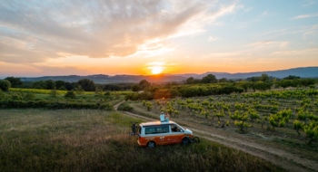 Couple sitting on a campervan standing at a wine field, looking into the sunset