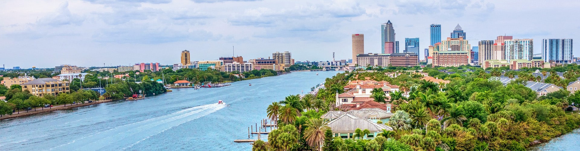 Island with houses built on it, in front of city skyline.