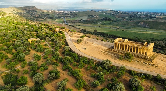 Historical temple in a sandy valley. Green hills and landscape in the background.