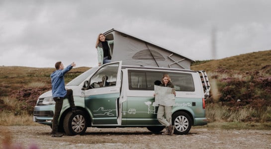 three friends around a campervan, looking for the right way with a map