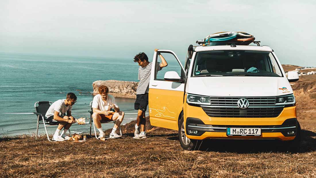 Three guys sitting and standing next to a campervan by the cliffs