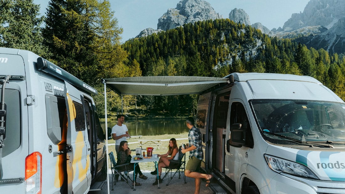 Two couples camping between two roadsurfer campervans, mountain scenery in the background
