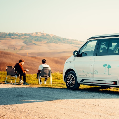 two friends sitting on chairs in front of campervan