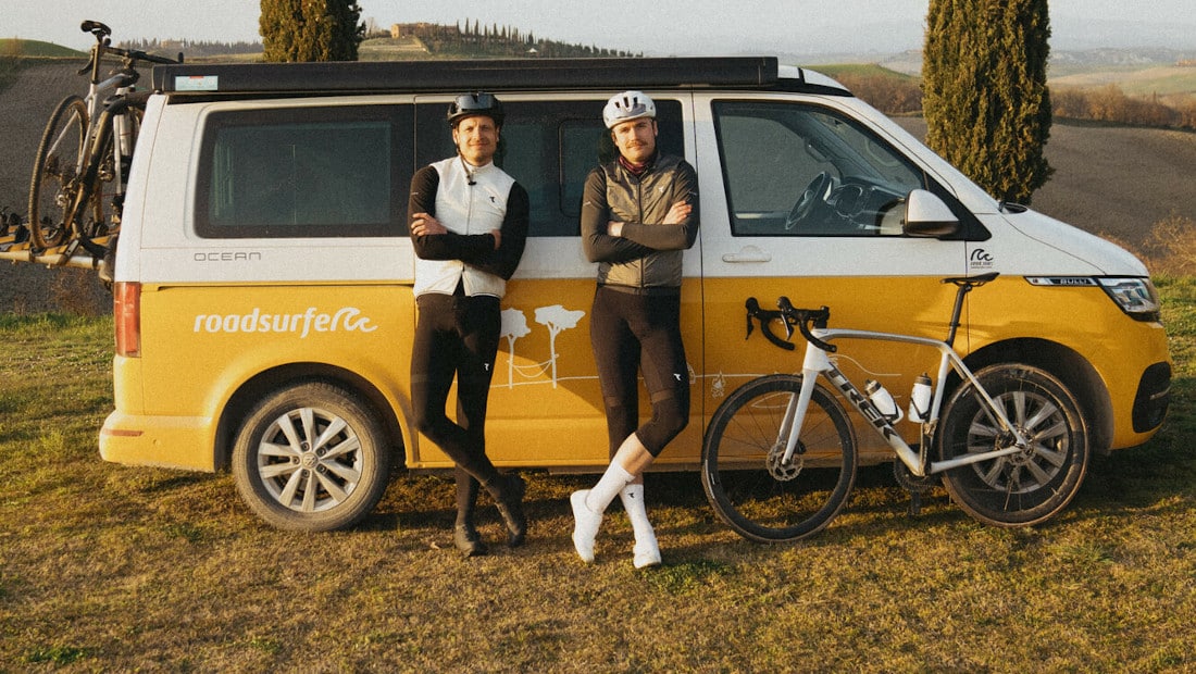 two friends with a bike posing in front of a yellow campervan