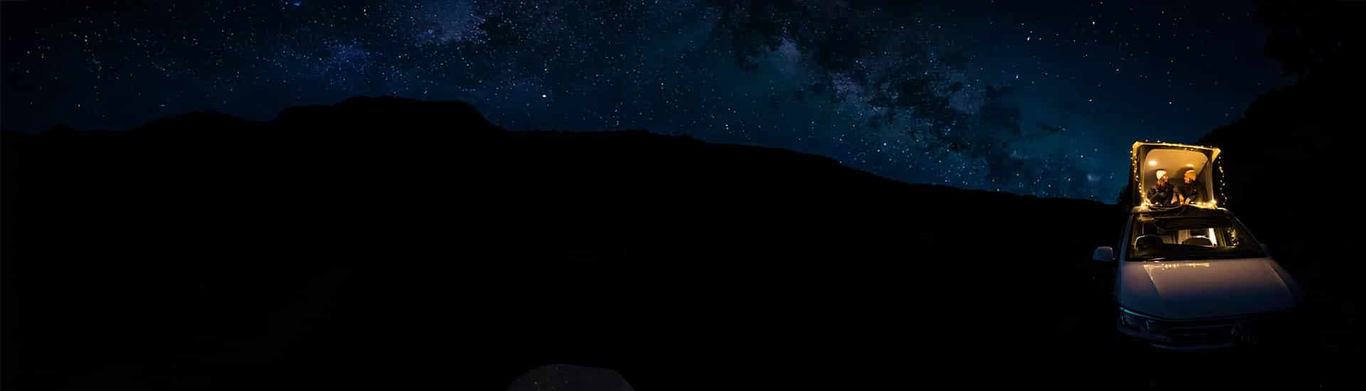 Two girls sitting in an open pop up roof of a campervan at night under starry sky