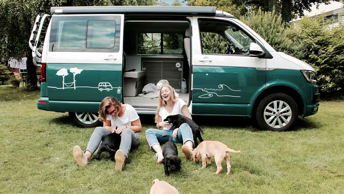two girls with puppies in front of a campervan