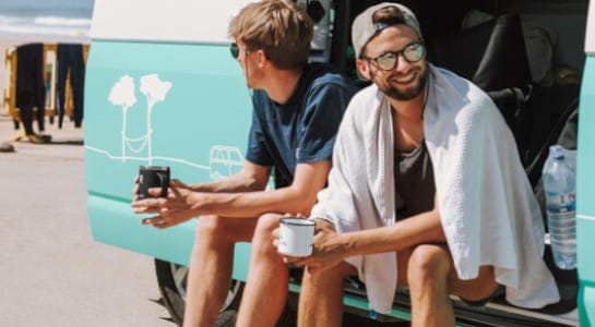 two guys sitting in a campervan with an open door with cups of coffee
