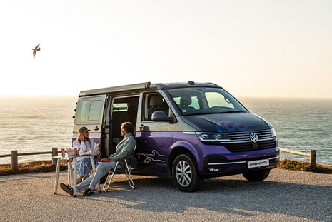 couple sitting in front of camper van at the sea