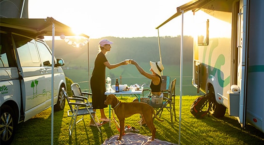 Two women clinking their glasses sat between to campers.