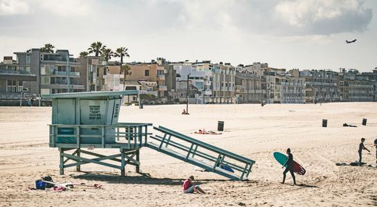 Lifeguard tower and surfers carrying boards along Venice Beach in Los Angeles