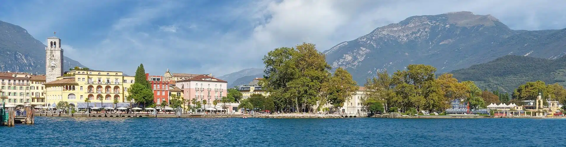 View over the lake garda in italy with the city and trees in the background. In the far back you can see the mountains and clouds in the sky.