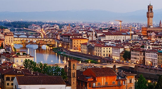 View over the rooftops of Florence and the river Arno at dusk with city lights