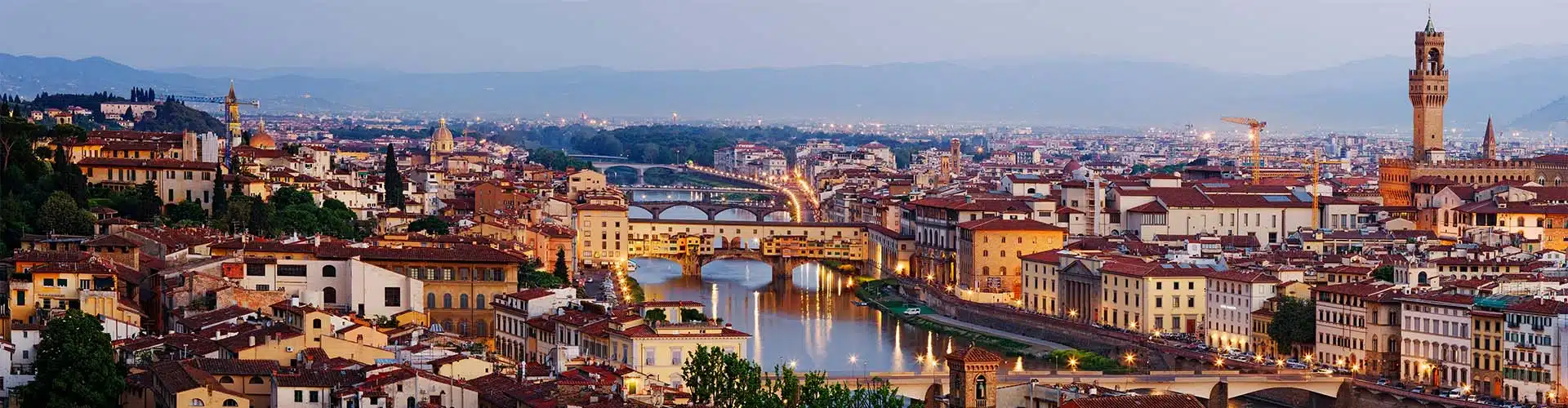 View over the rooftops of Florence and the river Arno at dusk with city lights