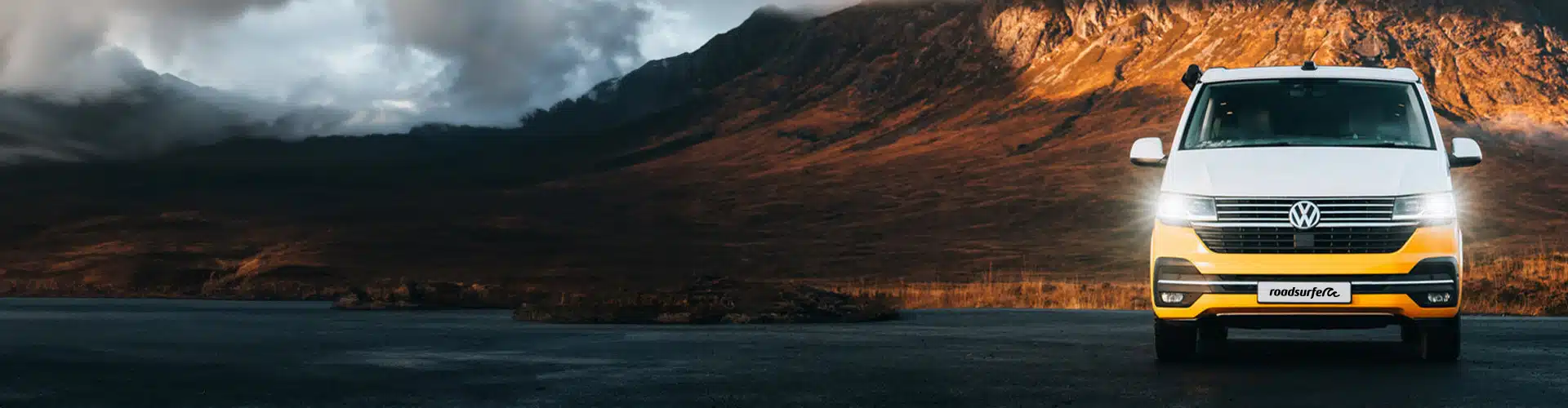 VW California Beach parking in front of a mountain with clouds 