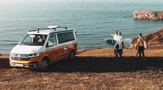 Three boys with surfboards and a roadsurfer vw california campervan at the beach