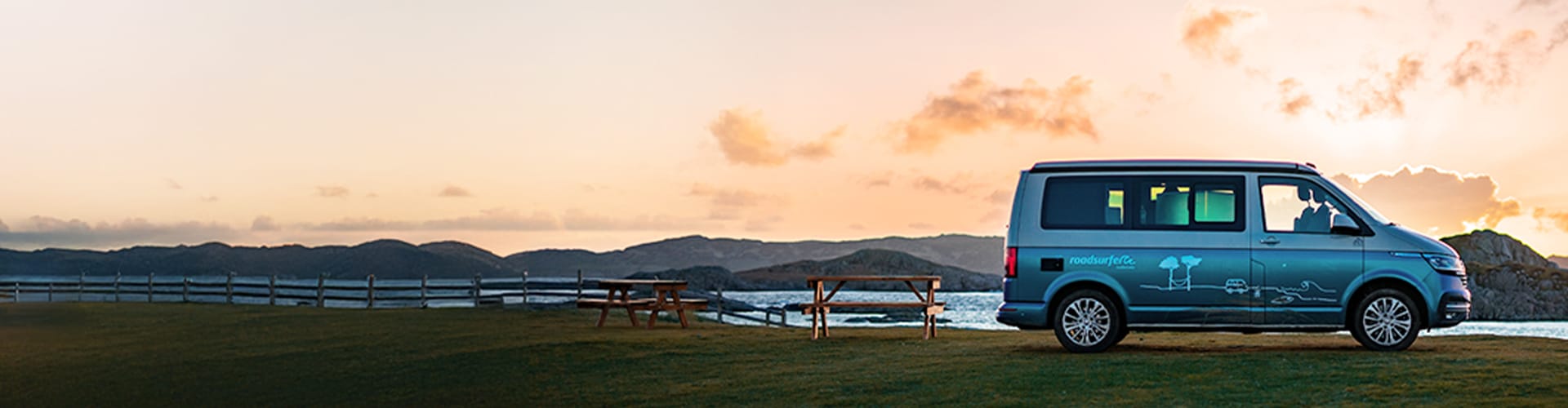camper van parked on a grassy area near a body of water at sunset, 