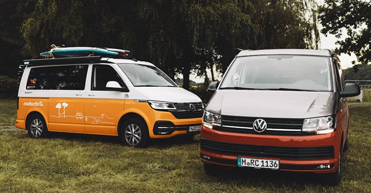 Red and yellow VW California Ocean campervans parked next to each other on grass.