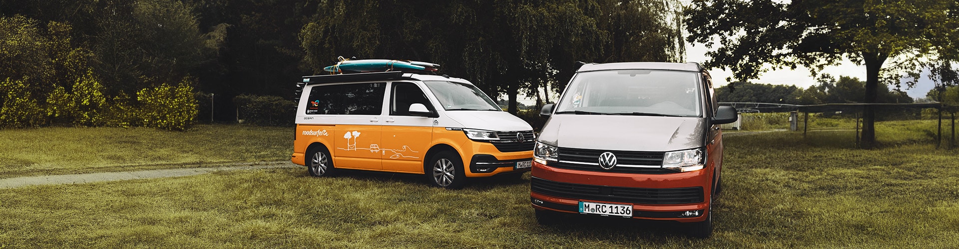 Red and yellow VW California Ocean campervans parked next to each other on grass.