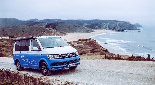 blue and white vw california on a road, beach in the background