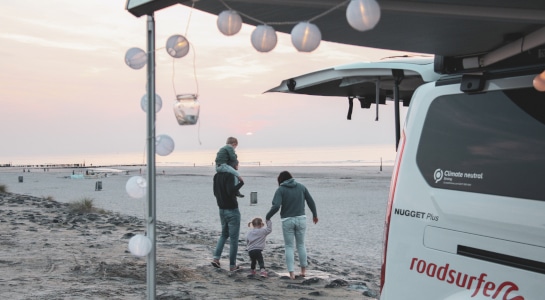 Family of four are camping on the beach with fairy lights strung on their vw campervan