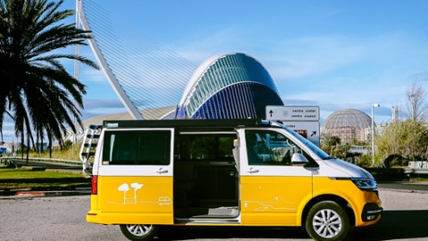 White and yellow campervan from roadsurfer standing in front of the Ciudad de las Artes y las Ciéncias in Valencia