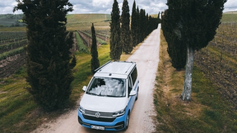 White and blue VW campervan from roadsurfer driving through a road in Italy