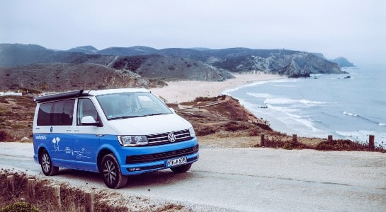 Blue and white VW California in front of a large beach in the Basque Country