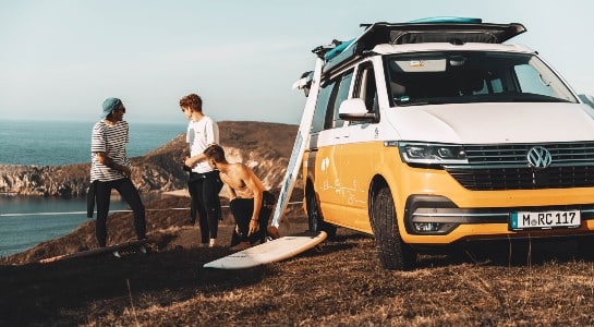Three youg guys preparing for surf in front of a yellow VW camper