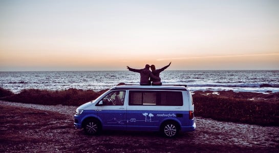 Couple sitting on a VW camper looking to the sunset at the beach