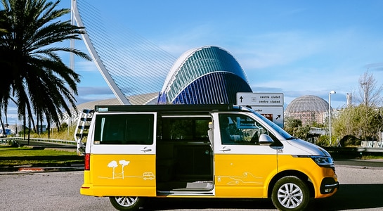 Yellow VW campervan from roadsurfer standing in front of the Ciudad de las Artes y las Ciencias in Valencia, Spain